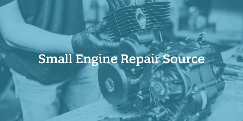 Hands holding a small engine sitting on a work bench