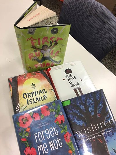 Books displayed on a table: "The First Rule of Punk," "Orphan Island," "The Hate U Give," "Forget Me Not," and "Wishtree."