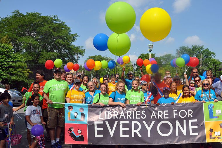 Library staff, board members, and friends holding Libraries Are for Everyone banner with balloons