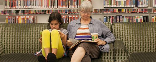 A girl and a woman reading on the couches at the library