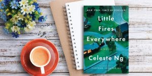 Little Fires Everywhere book on table with flowers, coffee mug, and notebook