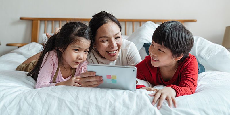 Parent and two kids with tablet on bed