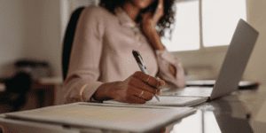 Person working on laptop and writing on paper with pen