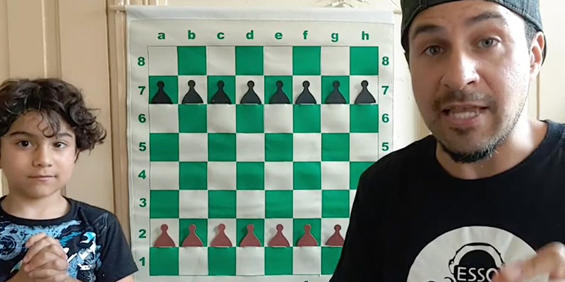 Video still showing adult and kid in front of a chessboard visual.