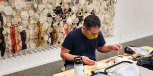 Artist works at table in front of artwork