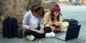 Two grade school students using a laptop to study outside