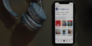 Media on Demand homepage with audiobook titles displaying on a smartphone with headphones sitting next to it