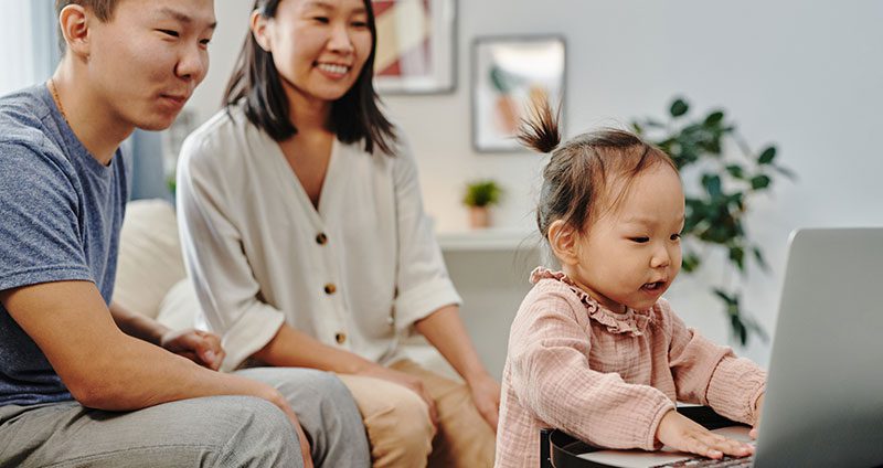 Young child using laptop while parents look on