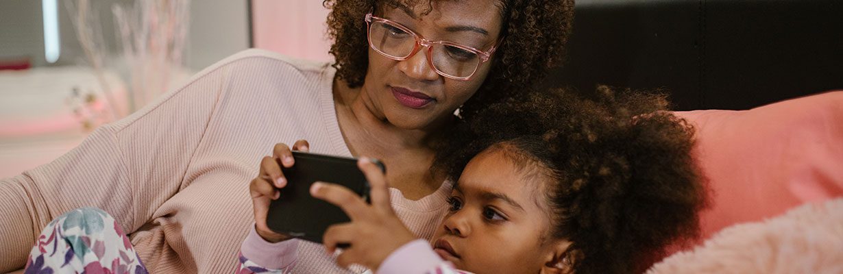 Child and adult playing with phone in bed