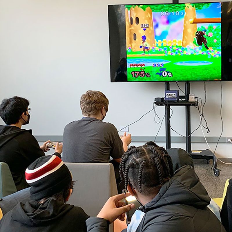 Teens playing video games on the big screen in the Teen Space