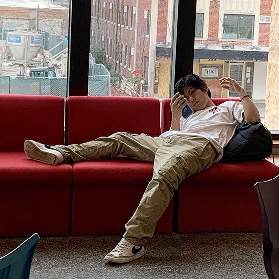 A teen looking at his phone while lounging on a couch in the Teen Space