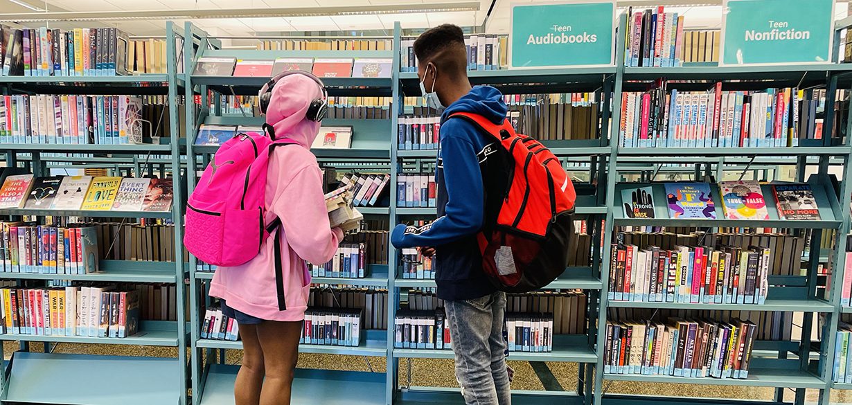 Two teens with backpacks looking at shelves of books