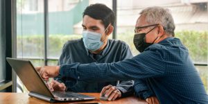 Two people wearing masks and working on a laptop