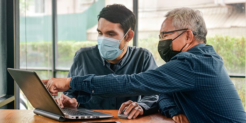 Two people wearing masks and working on a laptop