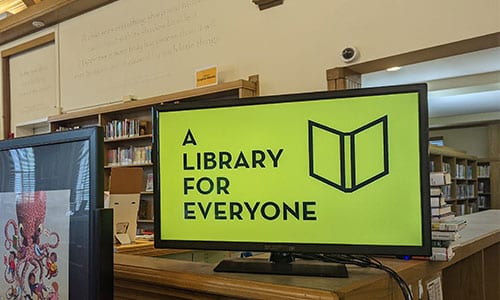 A computer screen at Maze Branch with the words "A Library for Everyone" and library book logo on yellow background