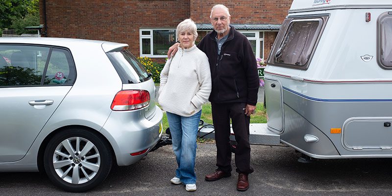 Older adults posing by a car pulling a camper