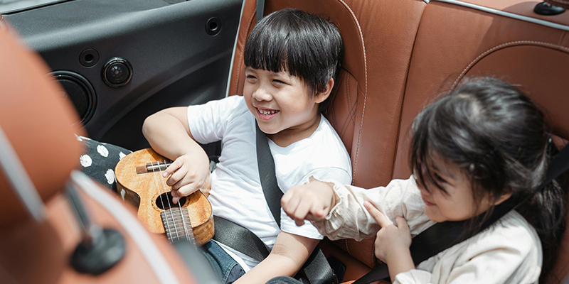 Two happy children sitting in the back of a car and playing a ukulele