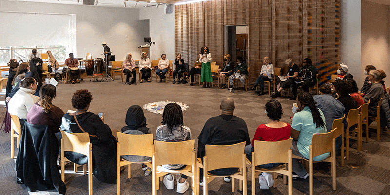 A large group of people sitting in chairs in a large circle in the library's Veterans Room