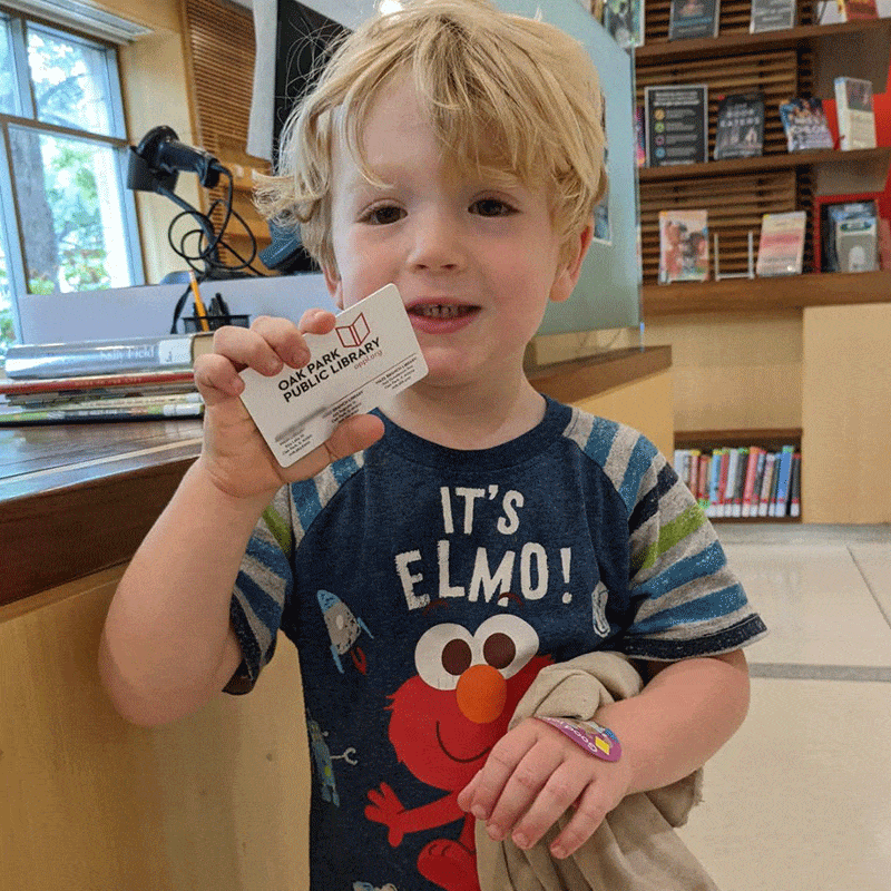 Young child holding library card, wearing Elmo shirt