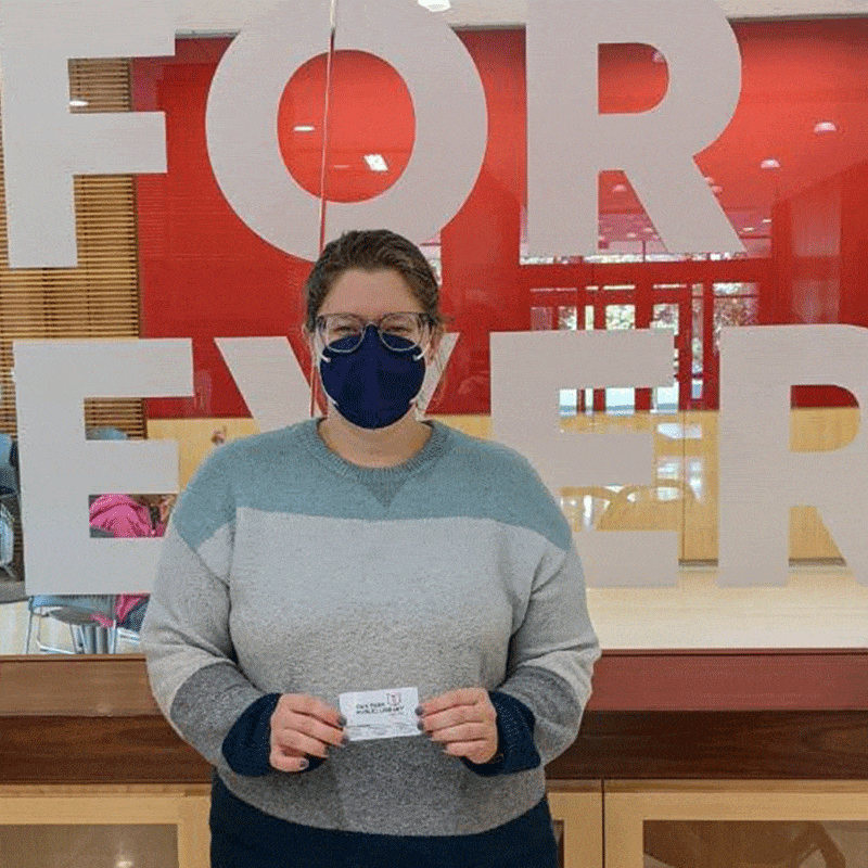 Person wearing mask shows off library card