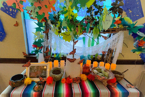 Ofrenda with candles, monarch butterflies, marigolds, bowls, framed photo