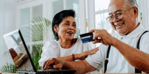 Two older adults laughing while using a laptop and holding a credit card