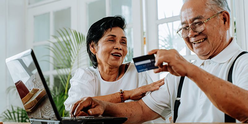Two older adults laughing while using a laptop and holding a credit card