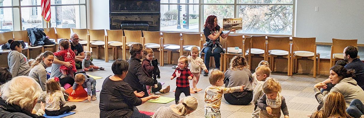 A lively storytime in the library with toddlers standing and moving throughout the room