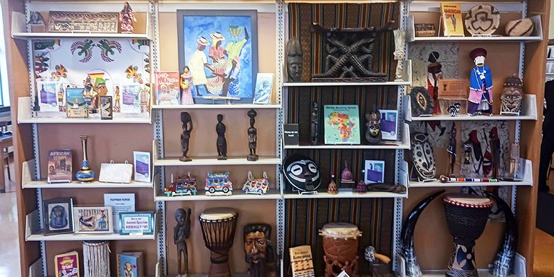 Multicultural Collection artifacts, including artwork, sculptures, drums, displayed on shelves