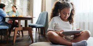 Kid using tablet with two adults in the background