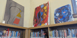 Three paintings by Chris Brown above the bookshelves at Maze Branch Library