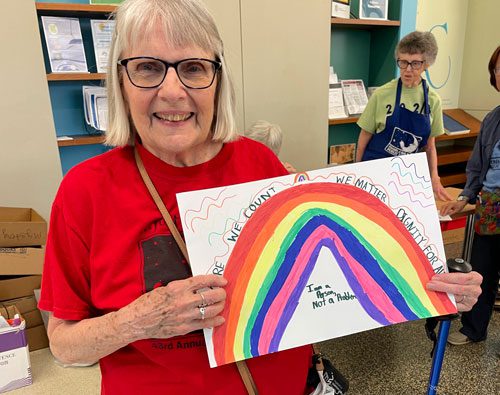 Woman holds sign for Disabiity Pride Month and a mobility aid