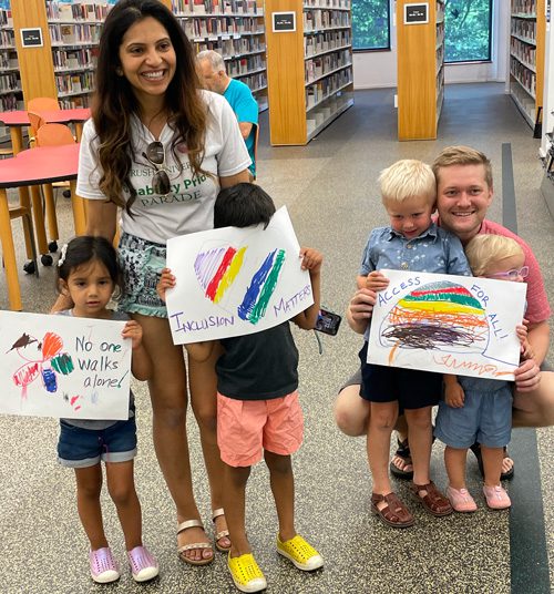 Two adults and four children pose in the library with signs they made for Disability Pride