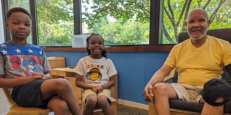 Robert Kelly and grandsons sit in chairs in the Main Library Children's Area