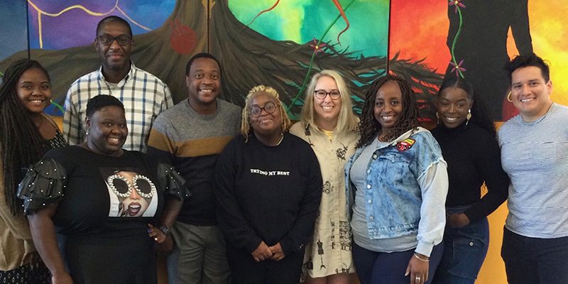 Group photo with Marché Pernell, Stephen Jackson, Dominique Hickman, Robert Simmons, Vann Harris, Ashley Knapp, Latonia Jackson, Synovia Knox, and Alexander Gutierrez in front of a wall mural