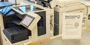 Printing sign with QR code sitting in front of printers at the Main Library