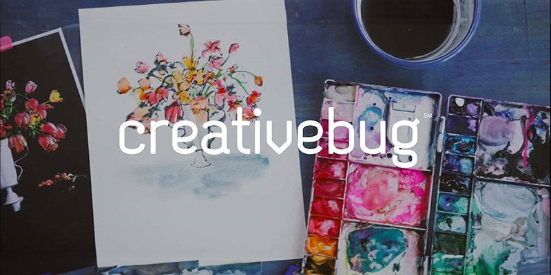 Creativebug logo on top of a table with a floral watercolor and painting supplies