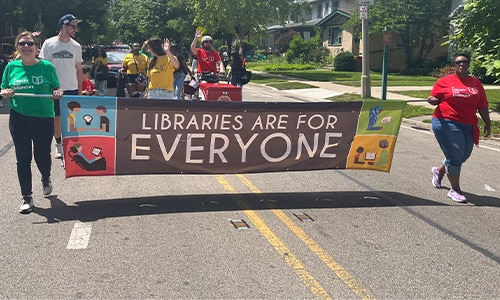 Library staff and board members march in the Juneteenth parade, holding a banner that reads "Libraries are for everyone"