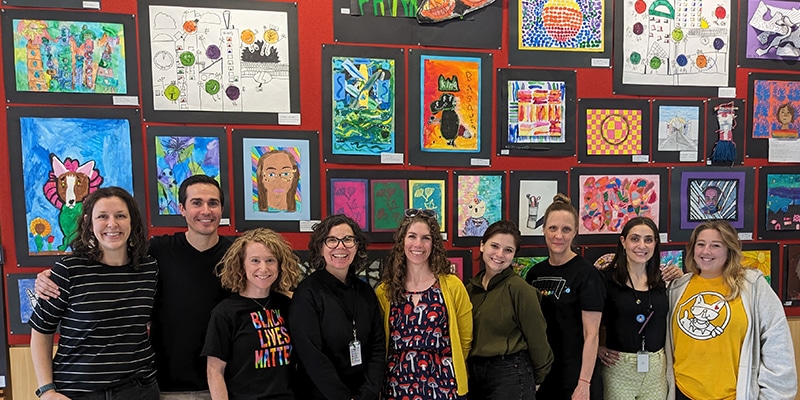 Oak Park Elementary School District 97 art teachers pose in front of a wall of student art in the Main Library