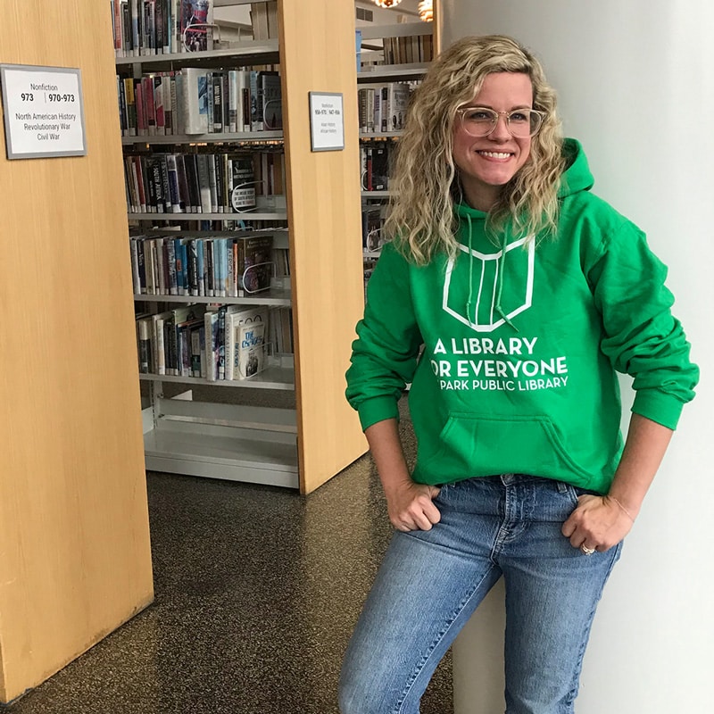 Person wearing green pullover sweatshirt with A Library for Everyone logo in library