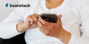 A person holds a phone with one hand and swipes the screen with the other. A logo for Beanstack is in the upper left.