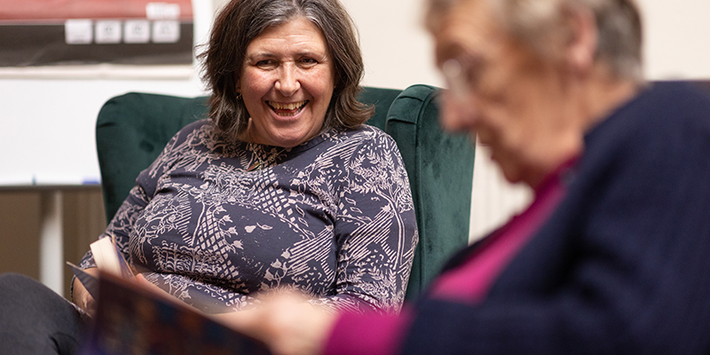 Two older adults participating in a book discussion, sitting in chairs, and holding books