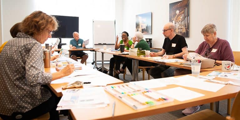 Older adults and library staff seated around a table chatting and drinking coffee