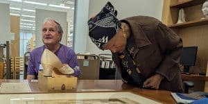 Two people in the Special Collections Reading Room. One examines a framed drawing on the table, another sits near a woman's heeled shoe