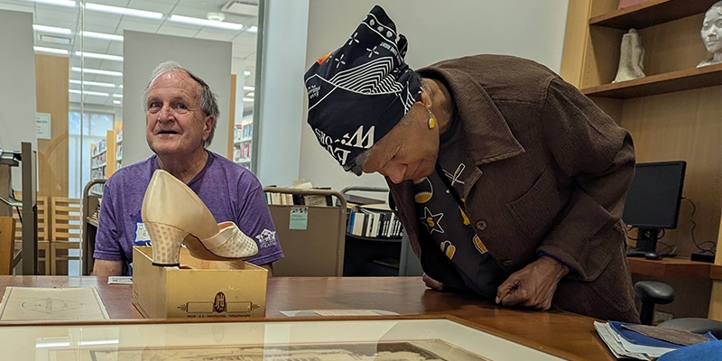 Two people in the Special Collections Reading Room. One examines a framed drawing on the table, another sits near a woman's heeled shoe