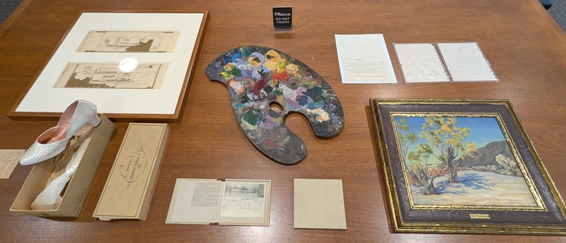 Framed drawings and a painting, a paint palette, women's heeled shoes, and papers on a table