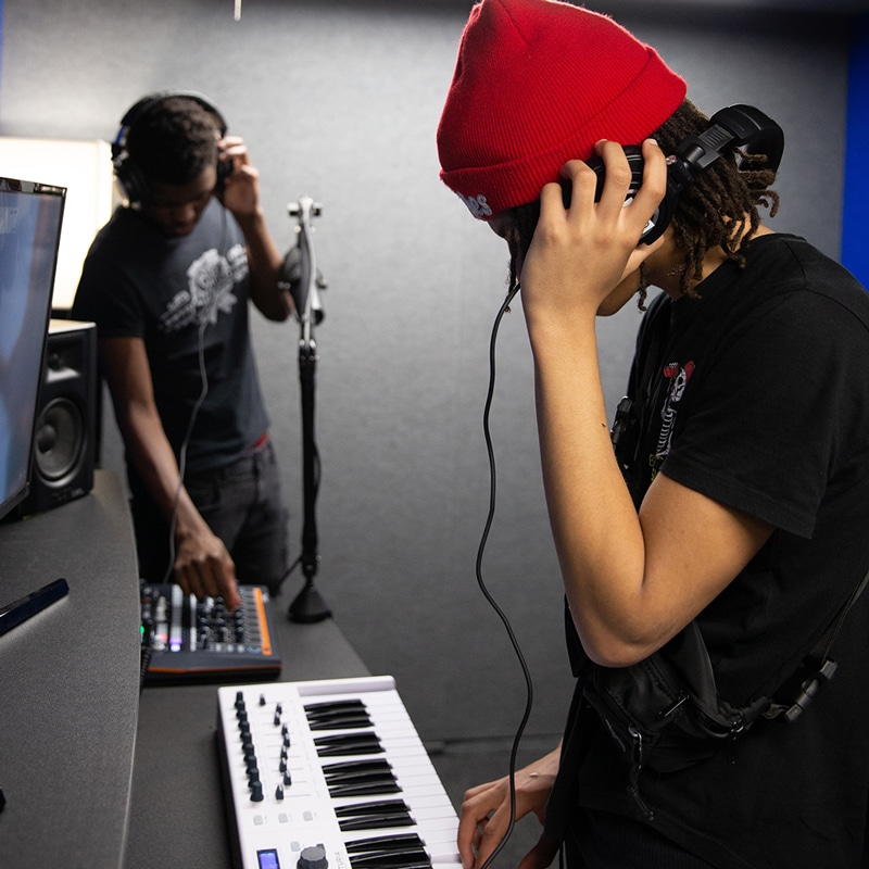 Two people in an audio booth with keyboard and headphones