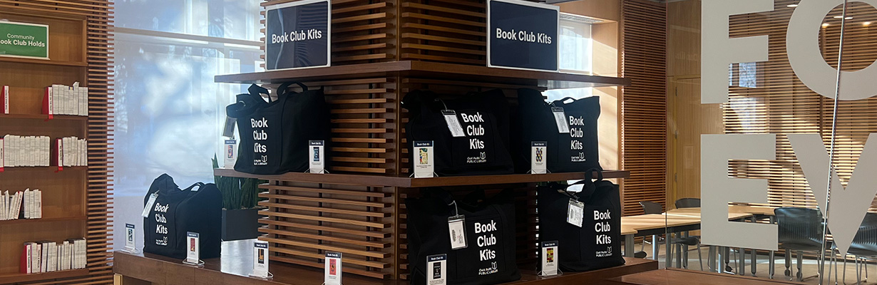 Shelf with black tote bags labeled Book Club Kit