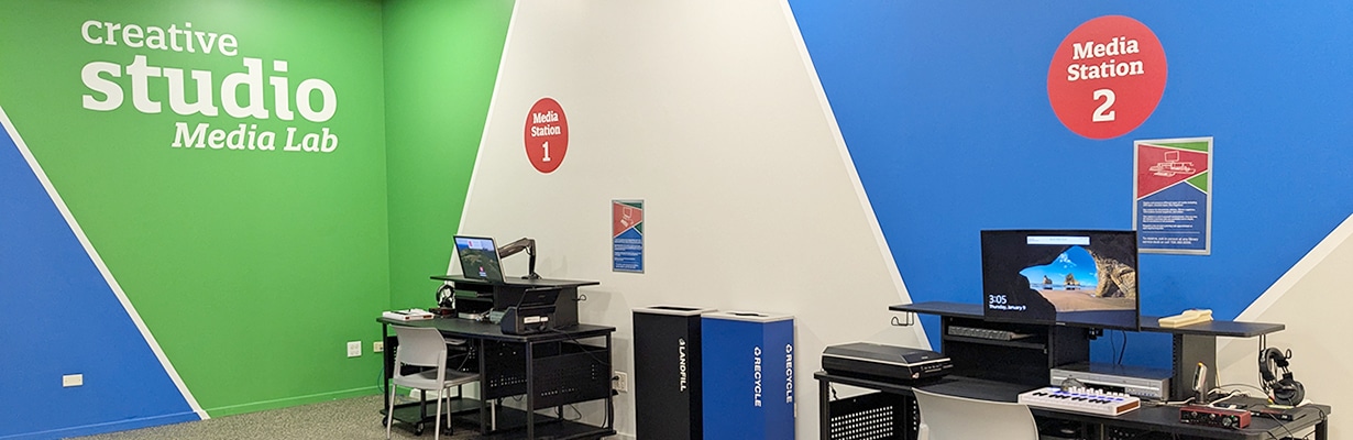 Two desks with digital equipment sitting alongside a wall with Creative Studio Media Lab displayed on it