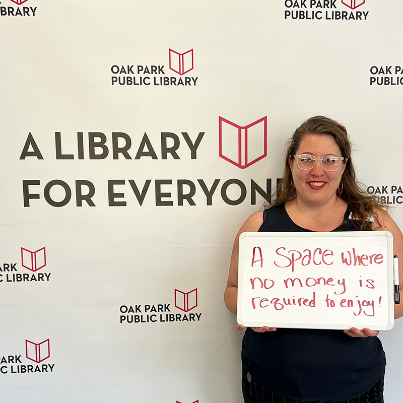 Library staff member holding a sign that reads, A space where no money is required to enjoy!
